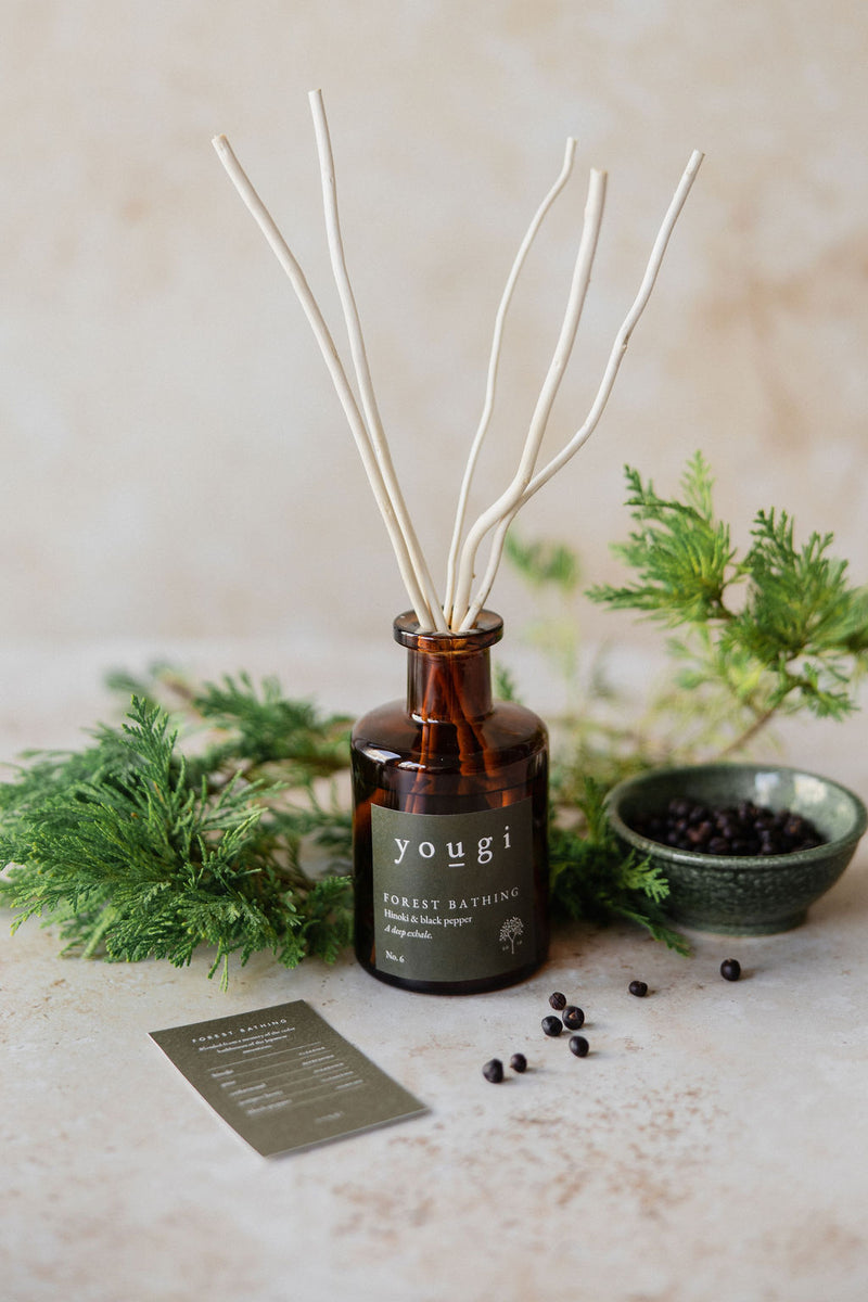 The Forest Bathing reed diffuser in amber glass with pine and a bowl of juniper berries