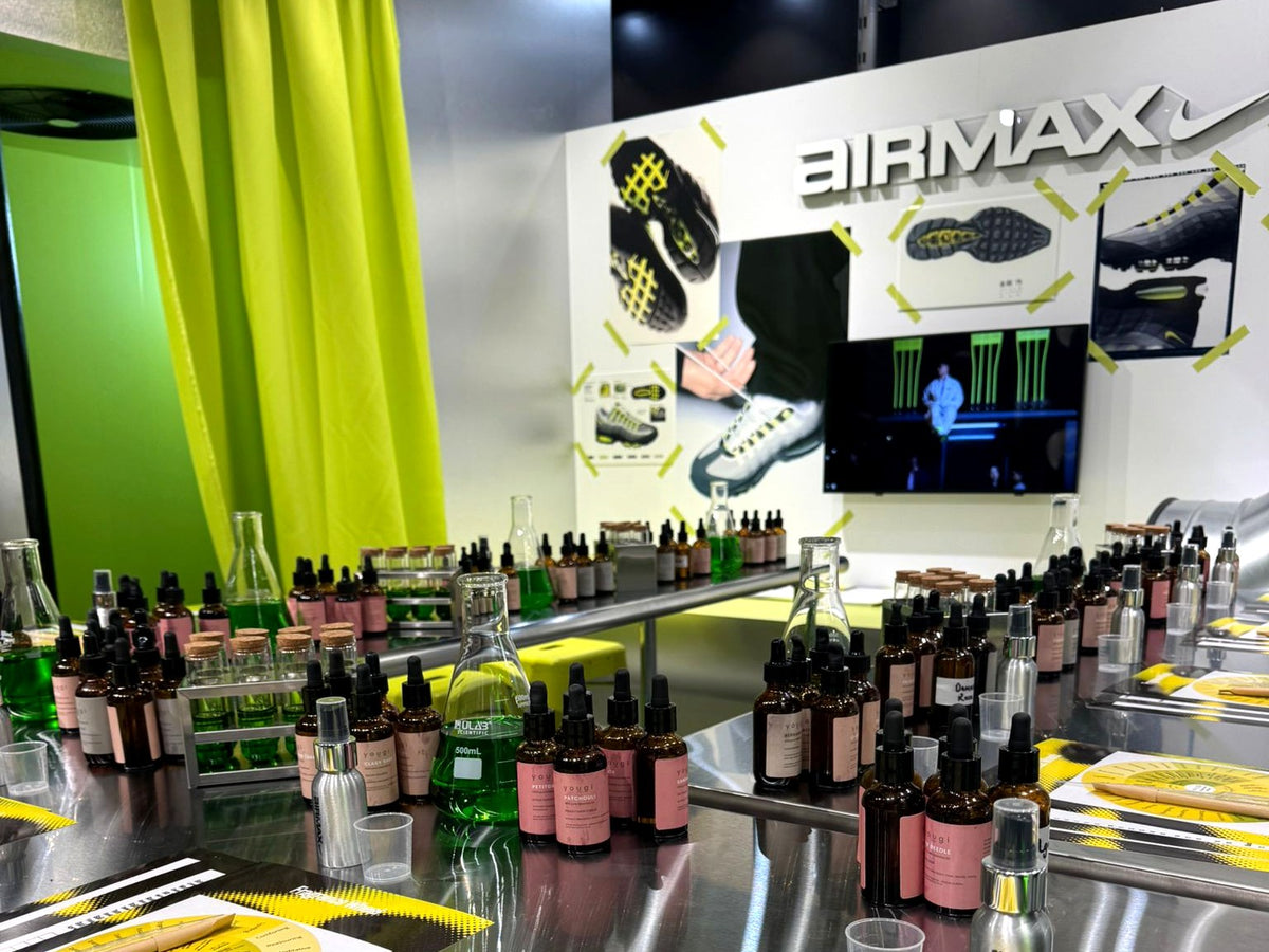 Yougi essential oils and perfumer's flasks on a steel bench with scent-wheel placemats, in front of a Nike Air Max branded wall