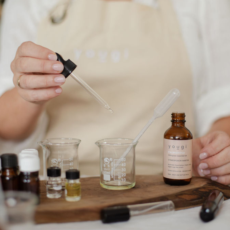 A hand adds essential oil to glass beakers on a wooden board in the Yougi studio.