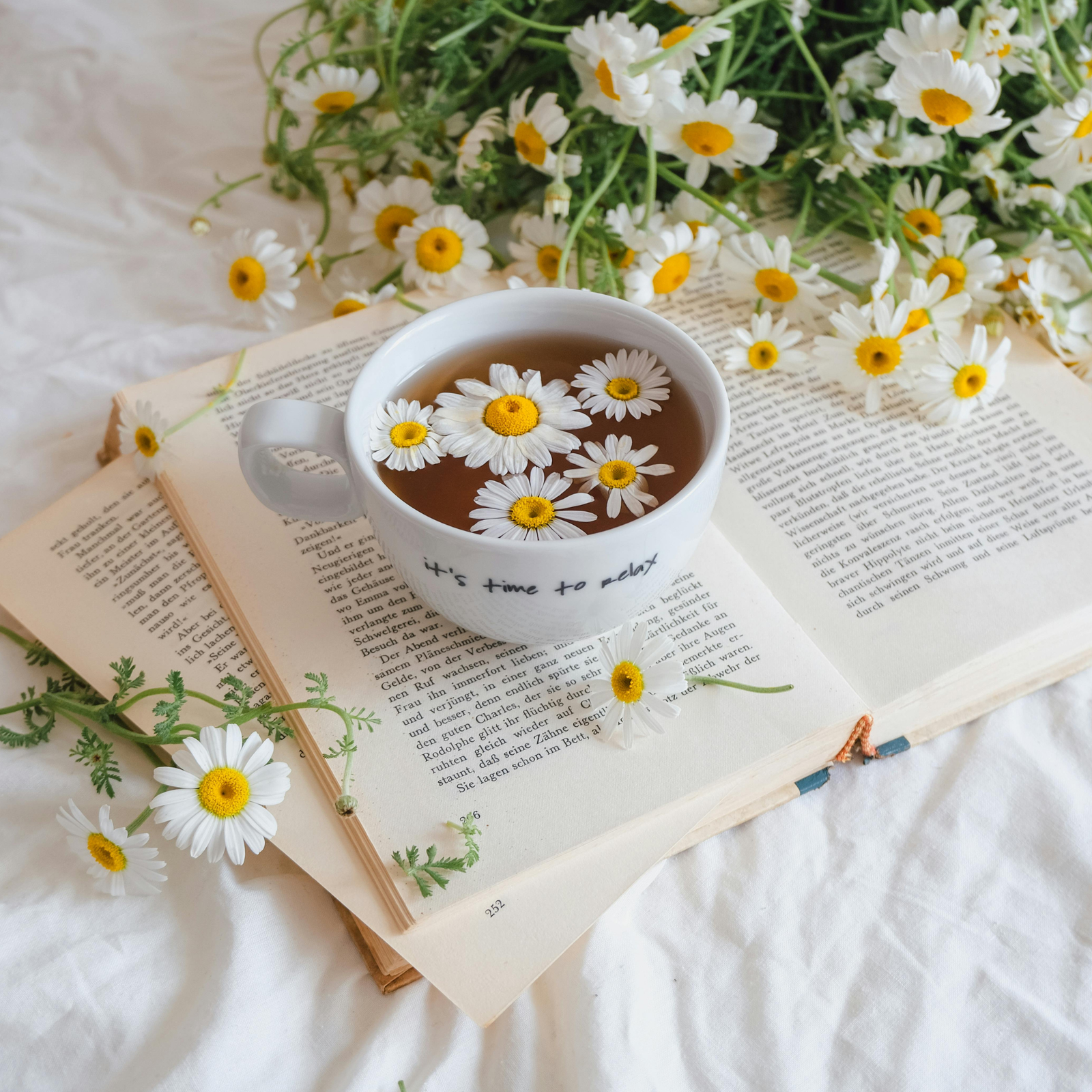 Chamomile flowers beside an amber essential oil bottle.