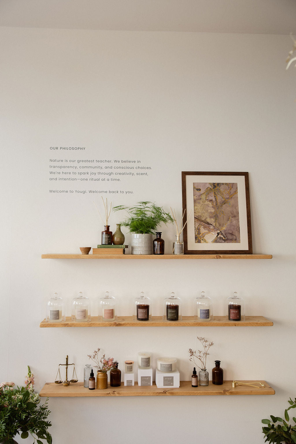 The shelves at 31 Connaught Street: Yougi candles under glass, oils, diffusers and a framed print on a white wall