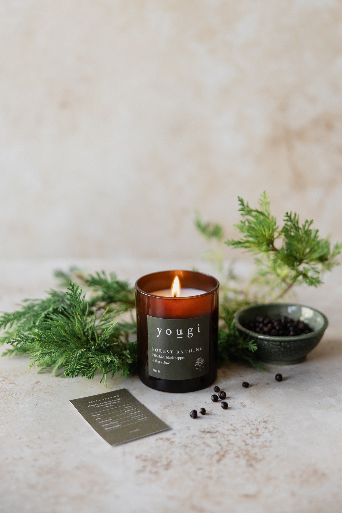 The Forest Bathing candle lit, in amber glass, with fir and juniper berries on stone