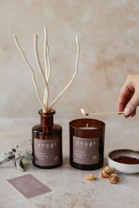 The Incense reed diffuser and candle in amber glass, a match held to the wick