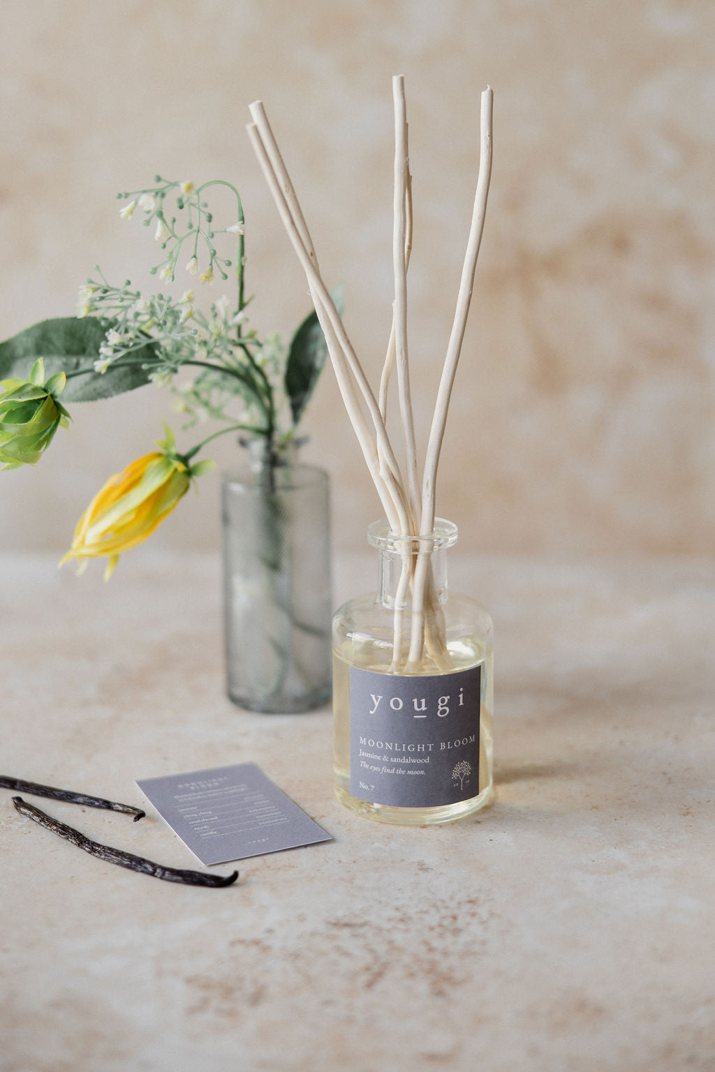 The Moonlight Bloom reed diffuser in frosted glass with yellow flowers and the scent card