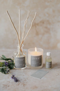 The Soothe reed diffuser, candle lit, and essential oil together on stone