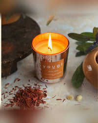 A lit Manifest candle beside sandalwood shavings, the frankincense, sandalwood and sage blend
