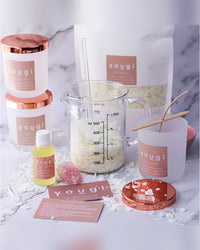 Candle-making kit laid out: eco soy wax, a 15ml essential oil blend, a measuring jug, frosted white glass vessels with copper lids and an instruction card