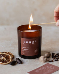 Hearth candle in amber glass being lit, with dried orange, nutmeg and clove