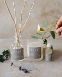 Soothe candle being lit beside its reed diffuser and essential oil, with lavender and eucalyptus