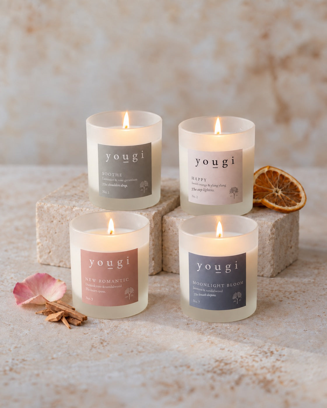 Soothe, Happy, New Romantic and Moonlight Bloom candles lit on stone blocks, with dried orange, a rose petal and sandalwood