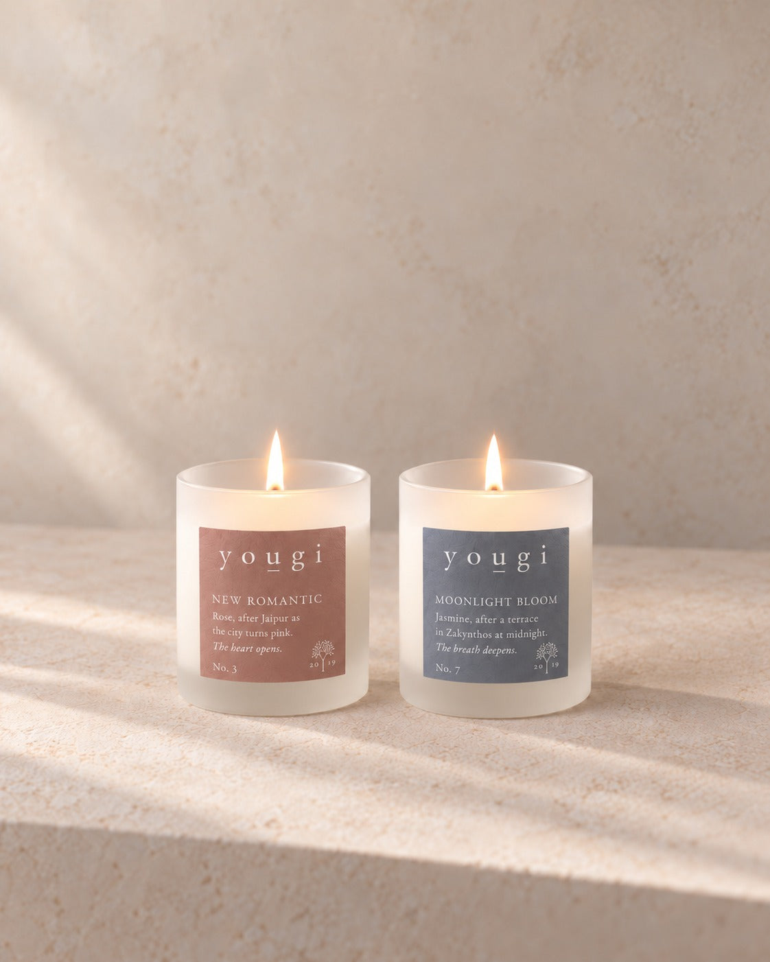 New Romantic and Moonlight Bloom candles lit side by side in frosted white glass, on stone