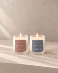 New Romantic and Moonlight Bloom candles lit side by side in frosted white glass, on stone