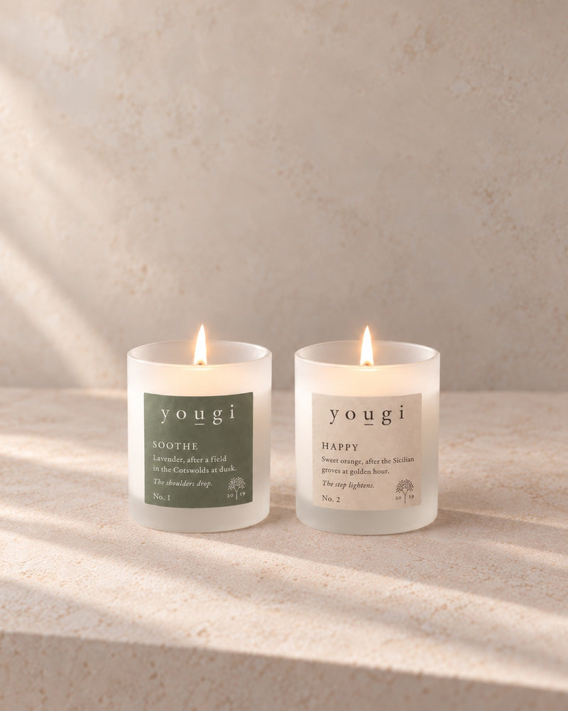 Soothe and Happy candles lit side by side in frosted white glass, on stone in morning light