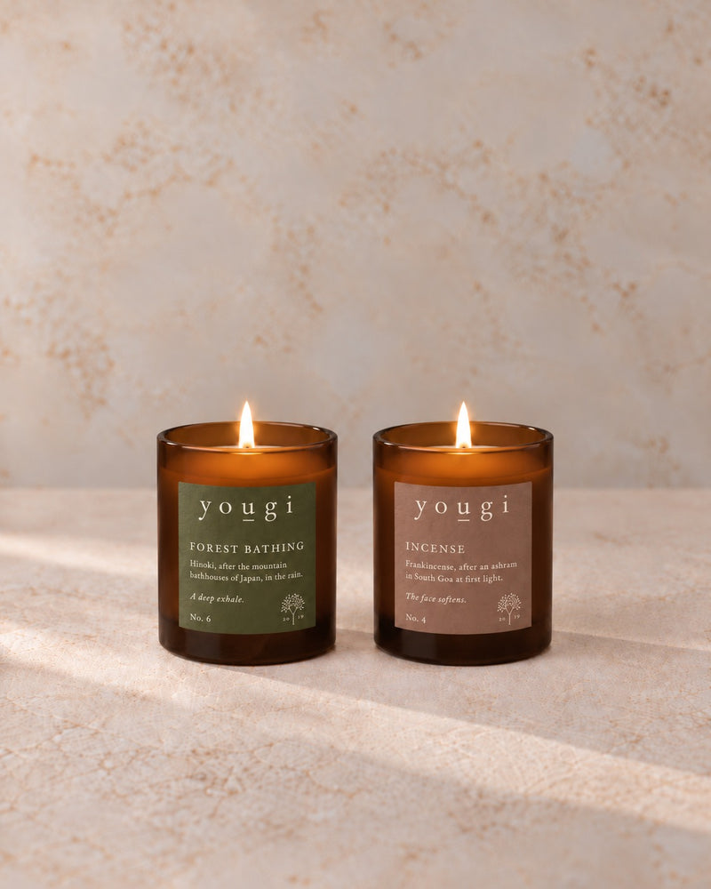 Forest Bathing and Incense candles lit side by side in amber glass, on stone